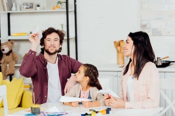 Adorable kid looking at father playing with paper plane at home — Stock Photo