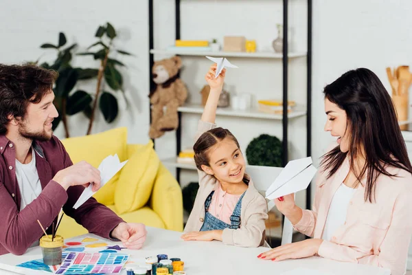 Glückliches Kind schaut Mutter beim Spielen mit Papierflieger in der Nähe des Vaters an — Stockfoto