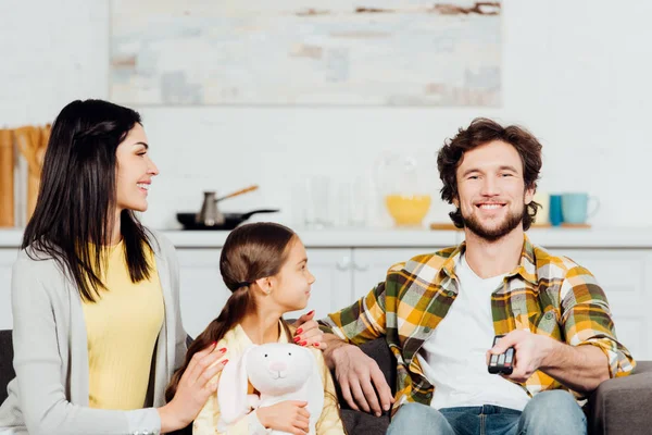 Alegre esposa e hija mirando hombre sosteniendo mando a distancia - foto de stock