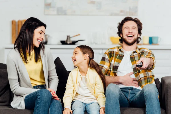 Счастливый отец смеется во время просмотра телевизора рядом с привлекательной женой и ребенком — стоковое фото