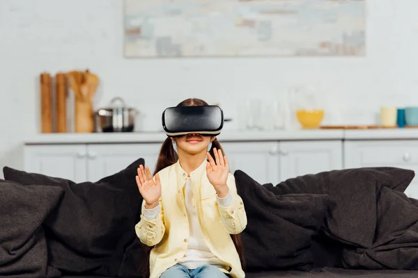 Niño alegre gesto mientras usa auriculares de realidad virtual en casa - foto de stock