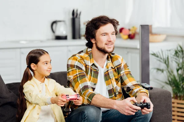 Lindo y feliz niño mirando padre sosteniendo joystick en casa - foto de stock