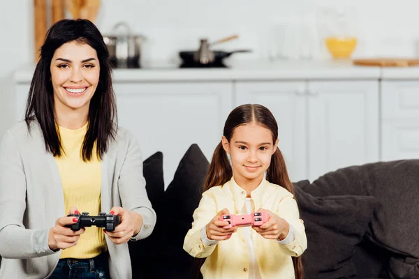 Happy kid playing with cheerful mother holding joystick at home — Stock Photo