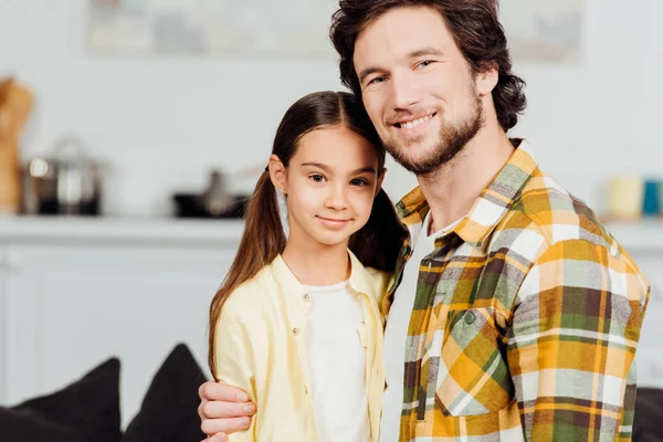 Glücklicher Vater blickt in die Kamera und umarmt glückliche Tochter zu Hause — Stockfoto