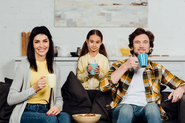 Happy family holding cups with drinks near bowl with tasty cookies — Stock Photo