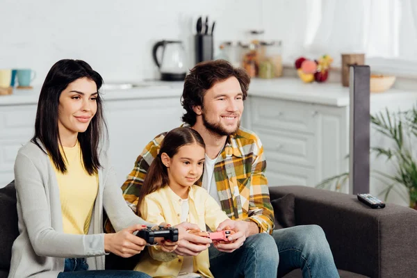 Felice uomo seduto vicino allegro bambino e moglie e giocare al videogioco a casa — Foto stock