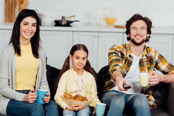 Uomo felice tenendo telecomando e tenendo tazza vicino alla famiglia — Foto stock