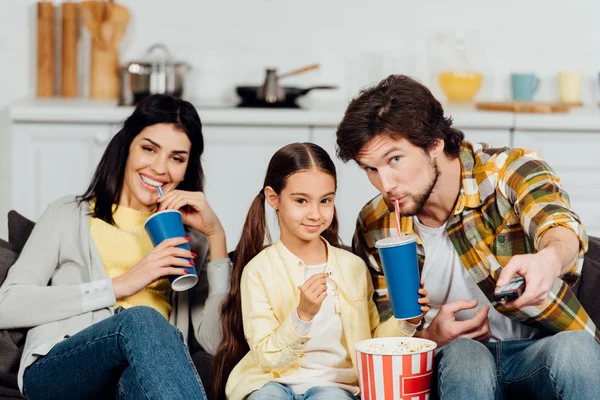 Bel homme buvant soda et tenant télécommande près de fille mignonne et femme — Photo de stock