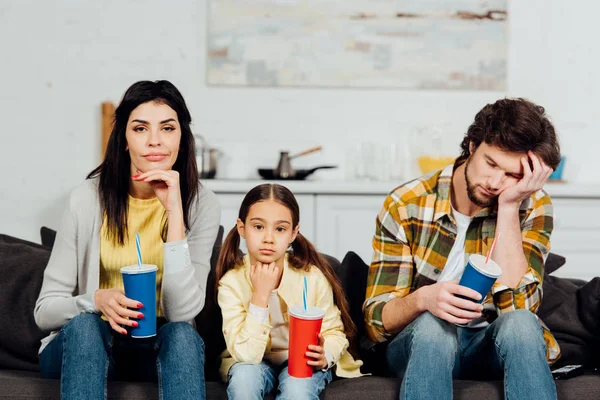 Famille ennuyée tenant des tasses jetables tout en regardant un film à la maison — Photo de stock