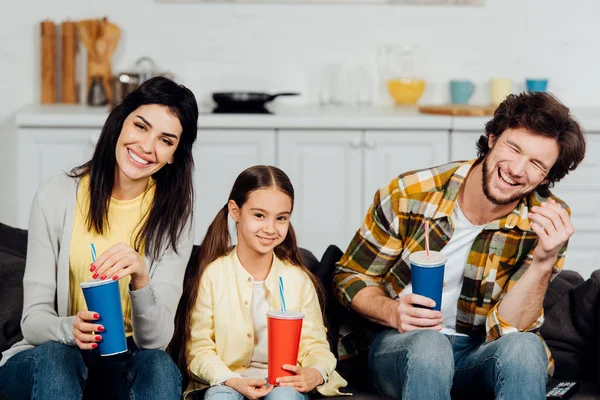Счастливая семья с пластиковыми чашками во время просмотра фильма дома — стоковое фото