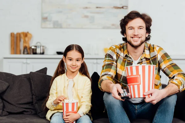 Feliz pai e filha assistindo tv e segurando baldes de pipoca — Fotografia de Stock