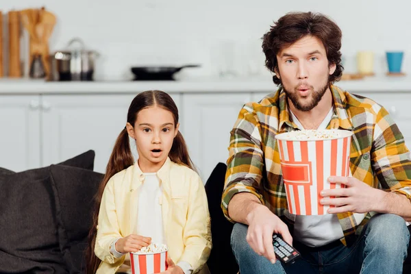 Surprised father and daughter watching movie and holding buckets of popcorn at home — Stock Photo