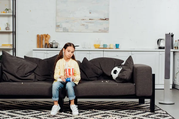 Verärgertes Kind schaut Meisterschaft und sitzt mit Eimer Popcorn auf Sofa — Stockfoto