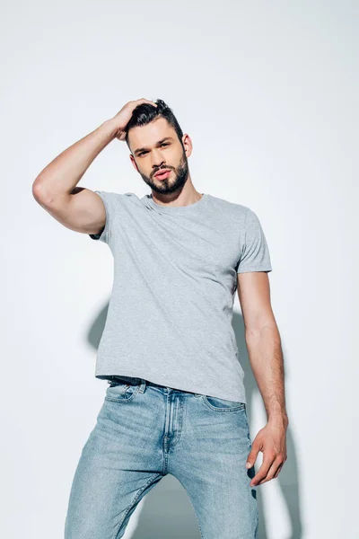 Vue à angle bas de bel homme touchant les cheveux et regardant la caméra sur blanc — Photo de stock