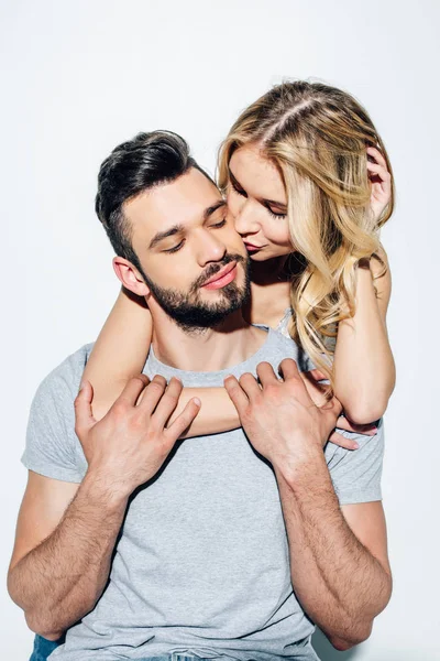 Attractive blonde girl kissing cheek of handsome bearded man in white — Stock Photo