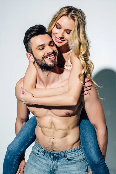 Glücklich hemdlos Mann huckepack fröhliche blonde Frau in Jeans auf weiß — Stockfoto
