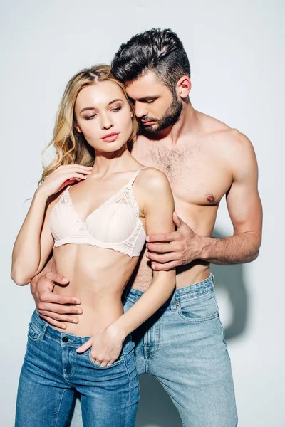 Shirtless man touching sexy blonde woman standing with hand in pocket on white — Stock Photo