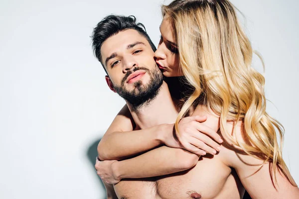 Блондинка целует щеку сексуального мужчины без рубашки на белом — стоковое фото