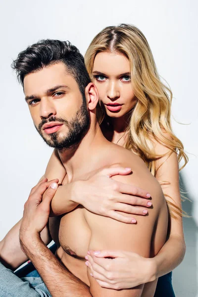 Femme blonde touchant beau petit ami torse nu et regardant la caméra sur blanc — Photo de stock