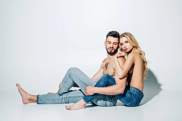 Attractive blonde girl hugging shirtless boyfriend while sitting on white — Stock Photo