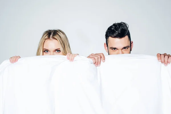 Femme blonde et homme regardant la caméra tout en couvrant le visage avec une couverture sur blanc — Photo de stock
