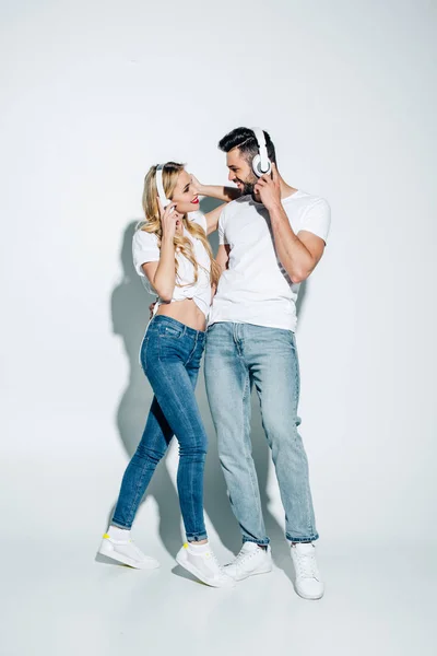 Glücklicher bärtiger Mann schaut attraktives blondes Mädchen mit Kopfhörern auf weißem Grund an — Stockfoto