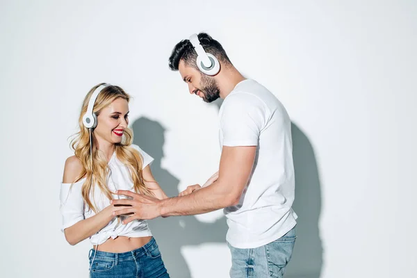 Glücklicher Mann mit Kopfhörern, der fröhliches blondes Mädchen auf weißem Hintergrund berührt — Stockfoto