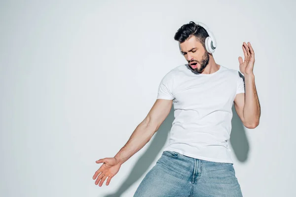 Hombre guapo escuchando música en auriculares y cantando en blanco - foto de stock