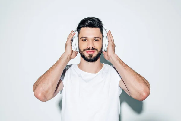 Uomo allegro che tocca le cuffie mentre ascolta musica e sorride sul bianco — Foto stock