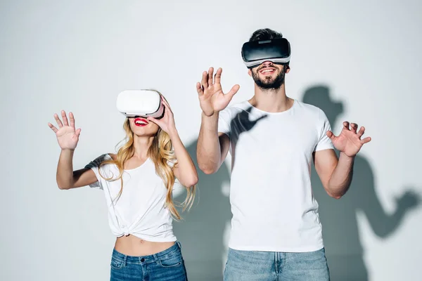 Веселый мужчина и женщина в наушниках виртуальной реальности жестикулирующие на белом — стоковое фото