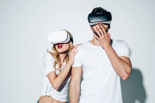 Homem e mulher surpresos vestindo fones de ouvido realidade virtual no branco — Fotografia de Stock