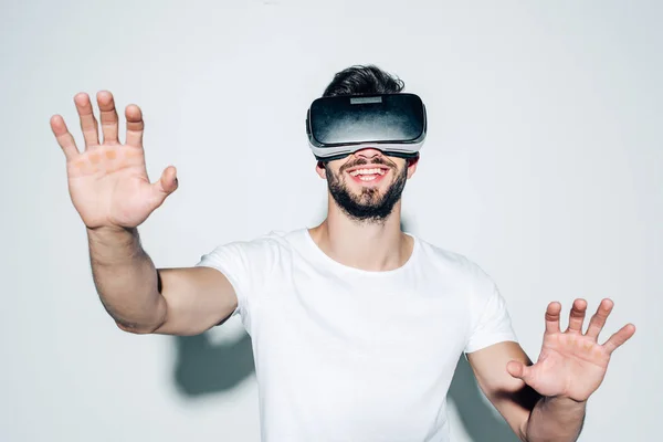 Cheerful bearded man wearing virtual reality headset while gesturing on white — Stock Photo