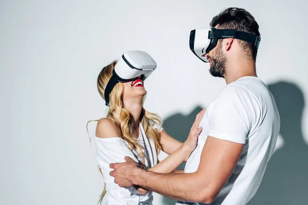 Hombre feliz tocando a la mujer rubia mientras usa auriculares de realidad virtual en blanco - foto de stock