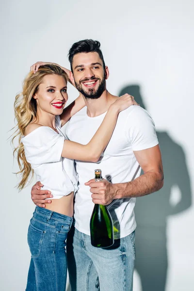 Mulher alegre abraçando homem feliz com garrafa de champanhe em branco — Fotografia de Stock