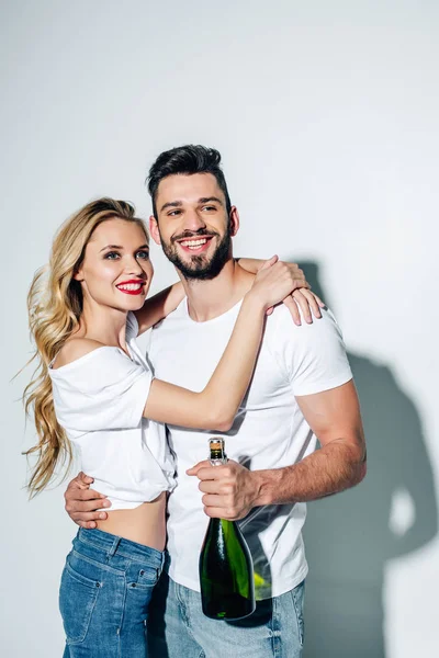 Cheerful young woman hugging happy man with bottle of champagne on white — Stock Photo