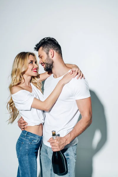 Heureux jeune femme étreignant bel homme avec bouteille de champagne sur blanc — Photo de stock