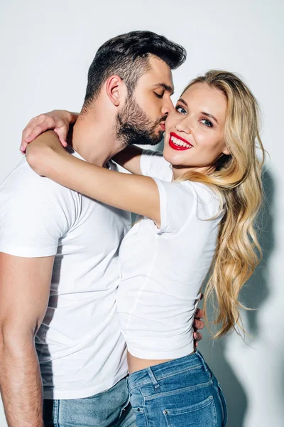 Handsome bearded man kissing cheek of happy blonde girl on white — Stock Photo