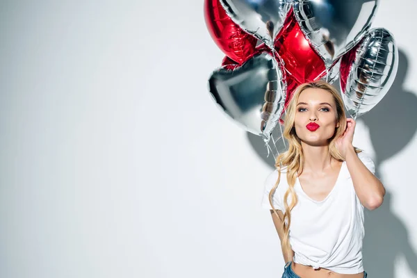 Attraente ragazza bionda con anatra faccia tenendo palloncini e toccando i capelli su bianco — Foto stock