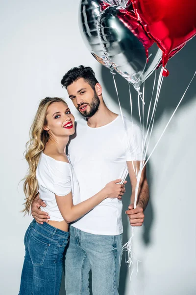 Cheerful woman hugging handsome man holding balloons on white — Stock Photo