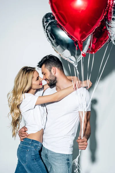 Cheerful blonde woman hugging handsome man with balloons on white — Stock Photo