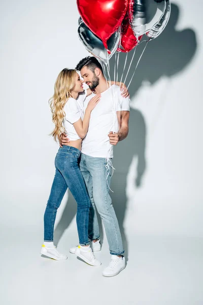 Cheerful blonde woman hugging handsome man standing in jeans with balloons on white — Stock Photo