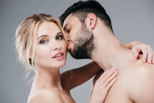 Handsome muscular man kissing cheek of attractive naked girl on grey — Stock Photo