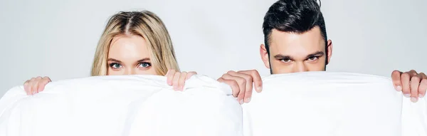 Panoramic shot of blonde woman and man looking at camera while covering face with blanket on white — Stock Photo