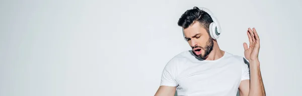 Panoramic shot of handsome man listening music in headphones and singing on white — Stock Photo