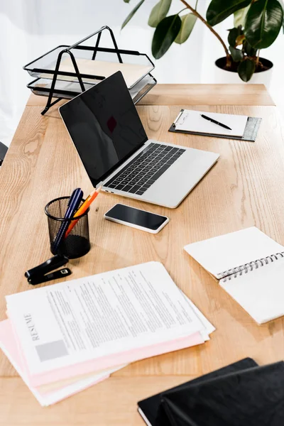 Современный офис со смартфоном, ноутбуком, резюме и чистым блокнотом на столе — стоковое фото