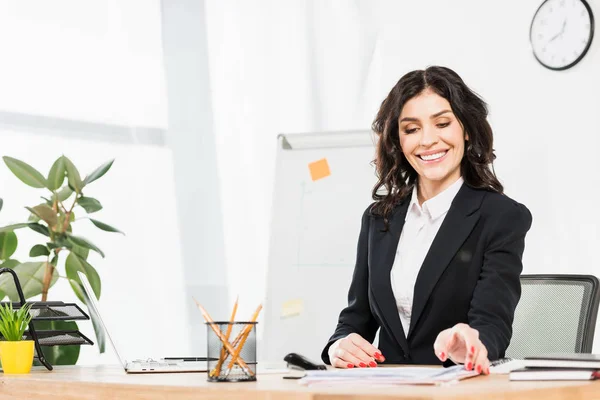 Happy brunette recruiter in formal wear looking at documents in office — Stock Photo