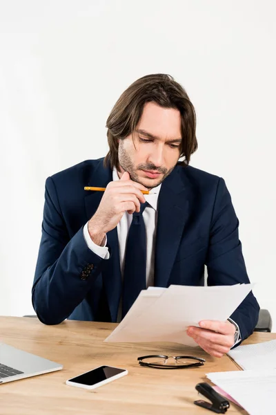 Gutaussehender Personalvermittler hält Papier in der Hand, während er im Büro neben dem Smartphone sitzt — Stockfoto