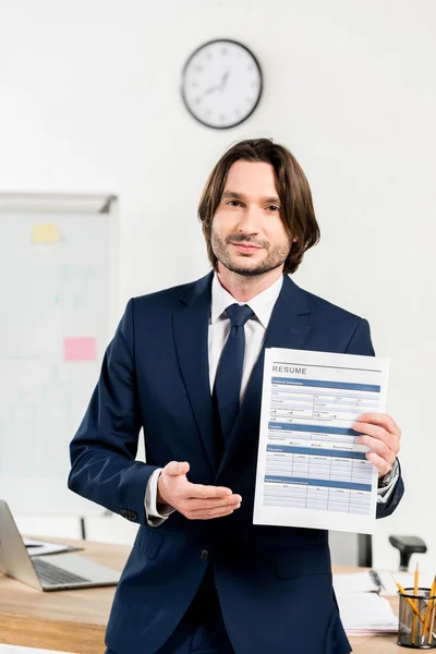 Bel homme en tenue formelle tenant CV et geste au bureau — Photo de stock