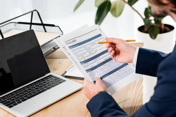 Selective focus of man holding resume and pencil near laptop with blank screen — Stock Photo
