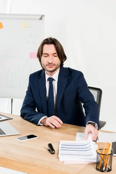 Gutaussehender Personalvermittler nimmt Lebensläufe auf, während er im Büro sitzt — Stockfoto